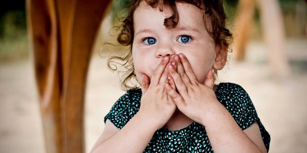 child holding hands in front of her mouth, as if to hide a secret