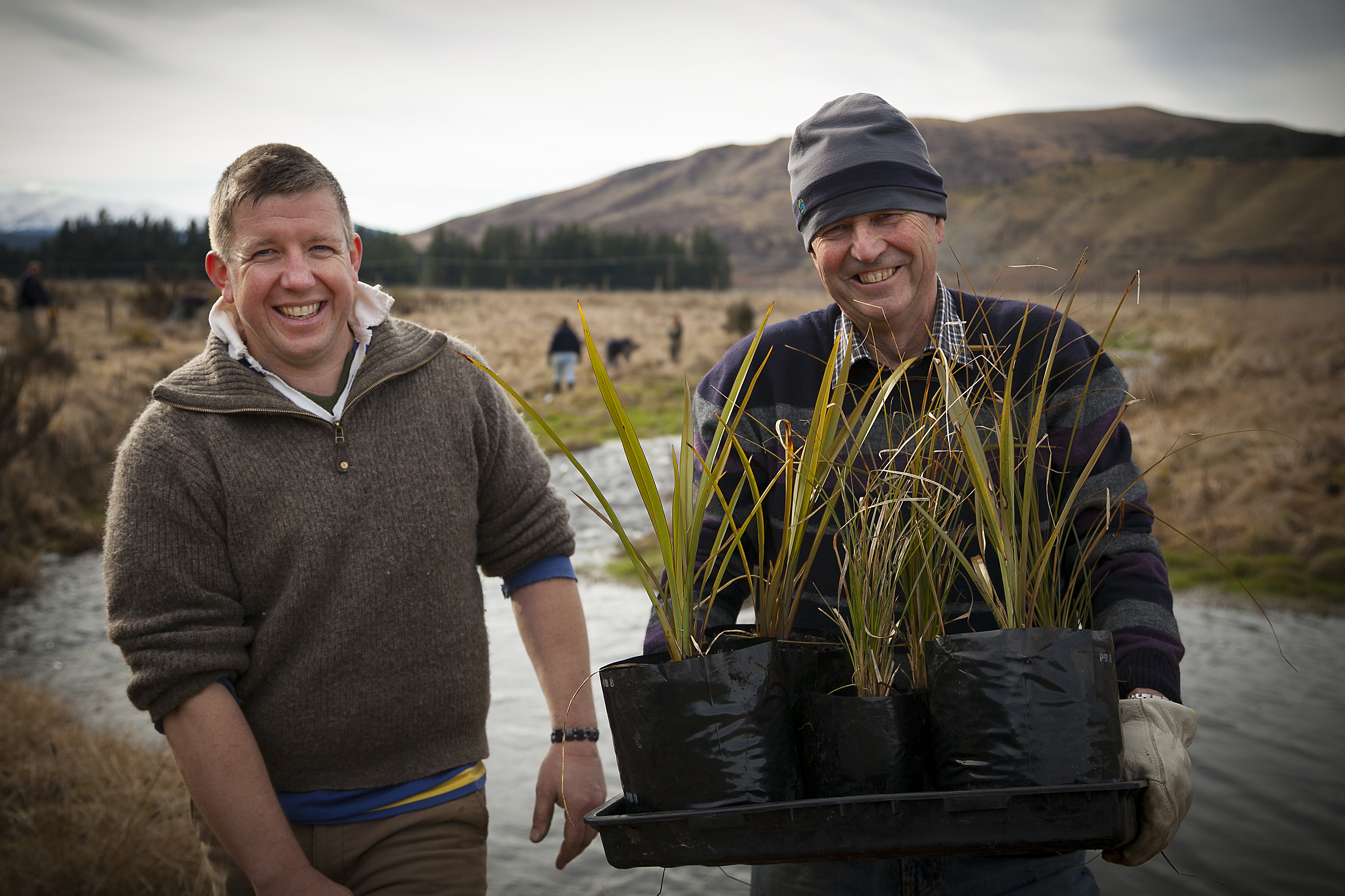 Two farmers holding plants in front of waterway