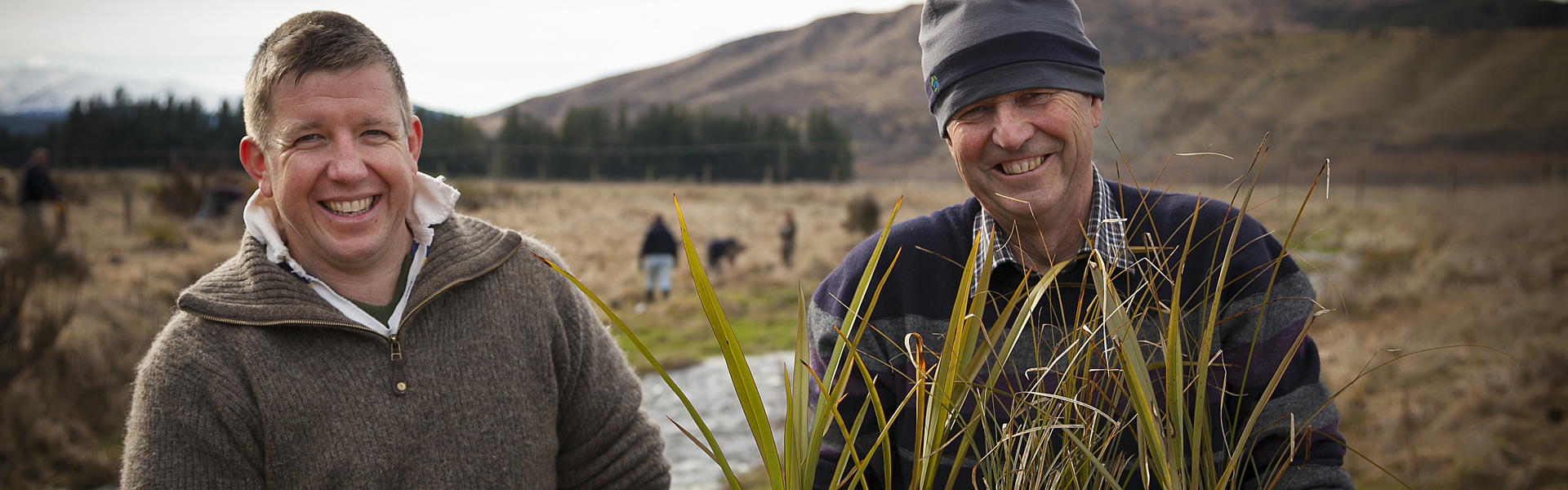 Two farmers holding plants in front of waterway