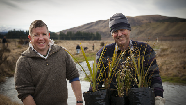 Two farmers holding plants in front of waterway