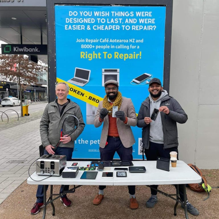 Three people in front of billboard promoting Right to Repair