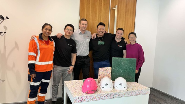 2 women and 4 men stand with their arms around in each other behind product made with reused material