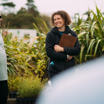 Woman holding clipboard smiling at man in front of flax plants
