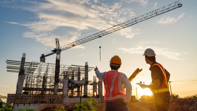 Two men in foreground of construction project and crane