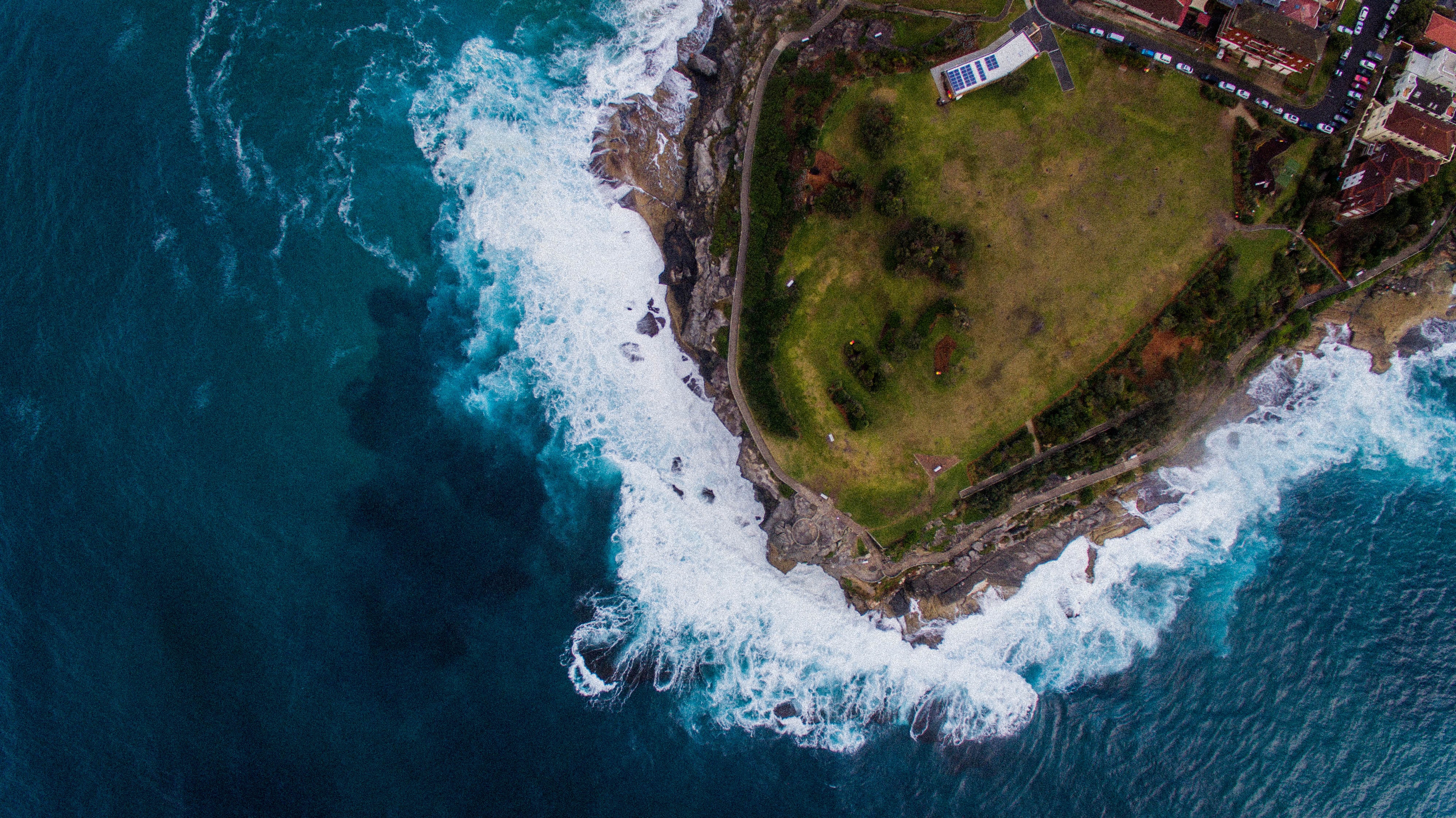 Drone image of waves crashing into grassy peninsula 