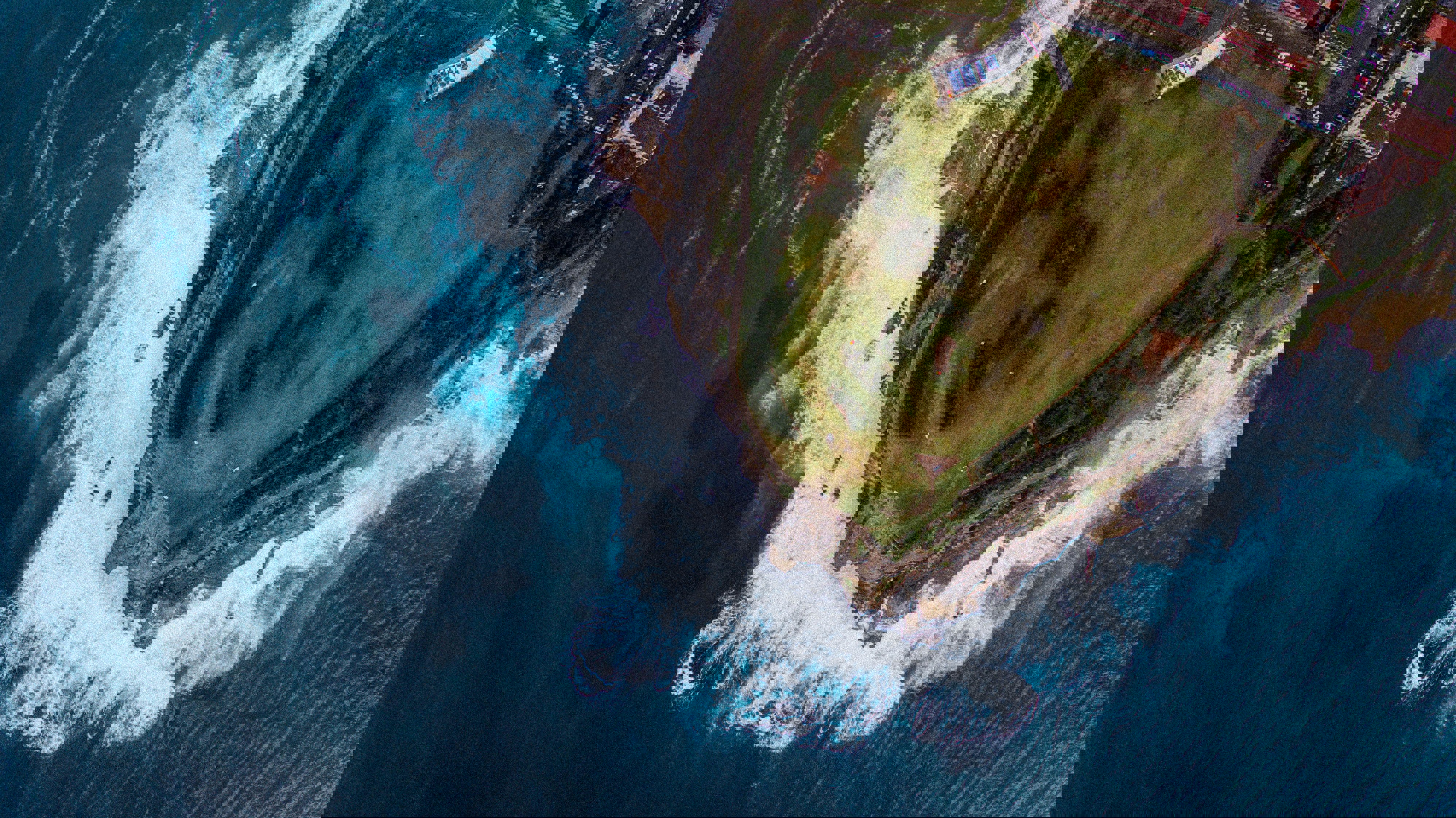 Drone image of waves crashing into grassy peninsula 