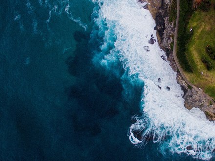 Drone image of waves crashing into grassy peninsula 